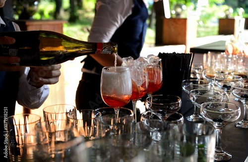  The bartender pours champagne into a glass to prepare a fashionable cocktail. Close-up with people's hands.