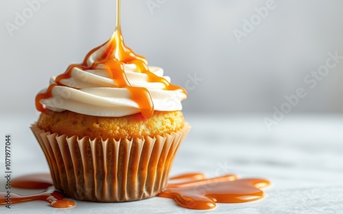 A single cupcake with white frosting is being drizzled with caramel on a white countertop