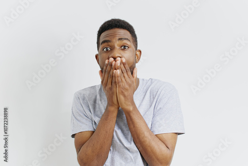 Surprised african american man covering mouth with hands isolated on white background expressing shock and amazement