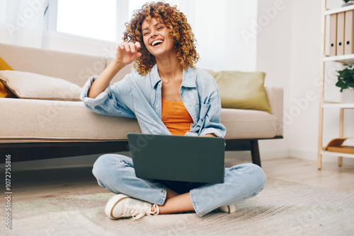 Smiling woman working with laptop in cozy home office, surrounded by modern technology and comfortable living room ambiance.