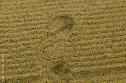 A relief trace of a sneaker on a soft surface of smoothed and cleaned sand with small furrows left over from tractor's harvesting attachments. Lifestyle holidays on beach, on vacation or on weekends