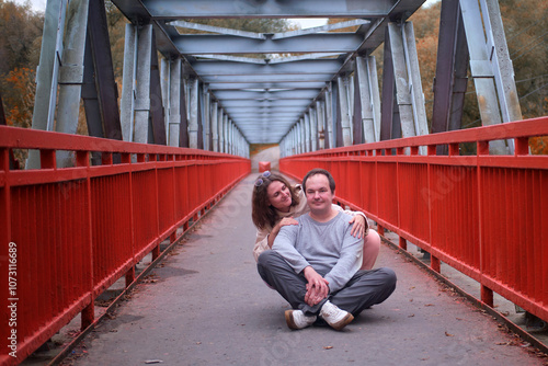 Man and woman sitting smiling on industrial girder bridge. Happy couple against urban constructions