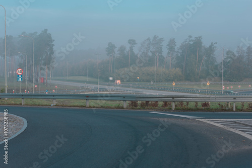 Węzeł drogowy przy autostradzie. Widać zjazdy i rozjazdy. Nad węzłem drogowy jak i nad pobliskim lasem unosi się mgła.