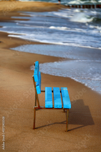 Niebieska ławka na żółtej plaży nad morzem. 