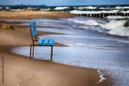 Niebieska ławka na żółtej plaży nad morzem. 