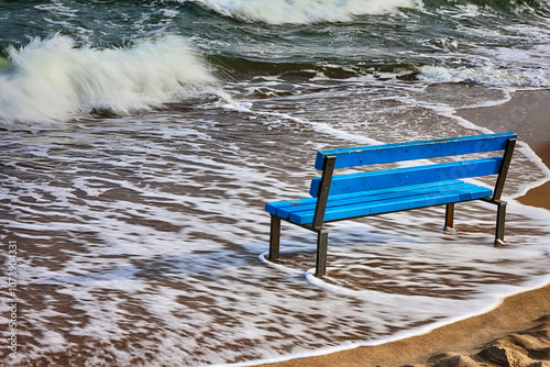 Niebieska ławka na żółtej plaży nad morzem. 