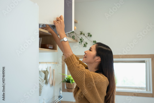 Beautiful woman reaching for ingredients in upper kitchen cabinets