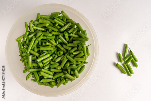 Fresh extra fine green topped beans cut nto smaller, manageable lengths, in a clear plastic bowl on white background