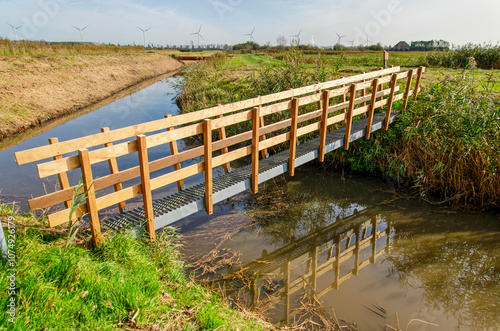 Narrow footbridge made out of steel and wood across a wide ditch in a polder landscape near Haarlem, The Netherlands