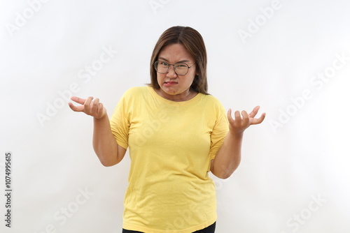 So what. Angry Asian woman raises eyebrows from annoyance keeps palms sideways shrugs shoulders with hesitation wears casual t-shirt isolated white background looks with bewilderment.