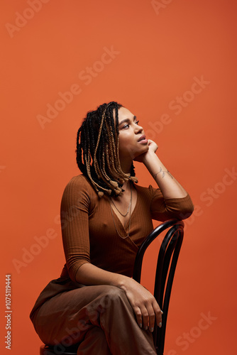 A young African American woman with stylish braids rests her chin on her hand, showcasing confidence and flair.