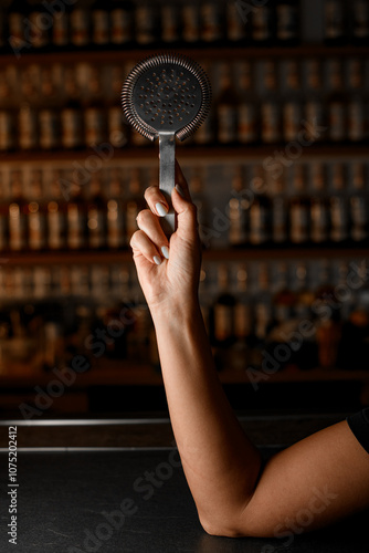 Female hands of bartender holding hawthorn steiner for straining cocktails while pouring into glass