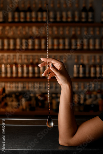 Female hands of a bartender holding a long golden bar spoon for mixing cocktails