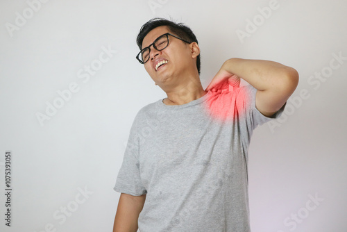 Adult Asian man touching his left shoulder with pain expression.