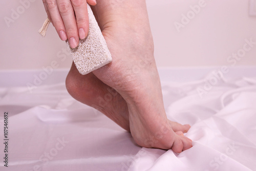 Woman using pumice stone for removing dead skin from feet. Dry feet.