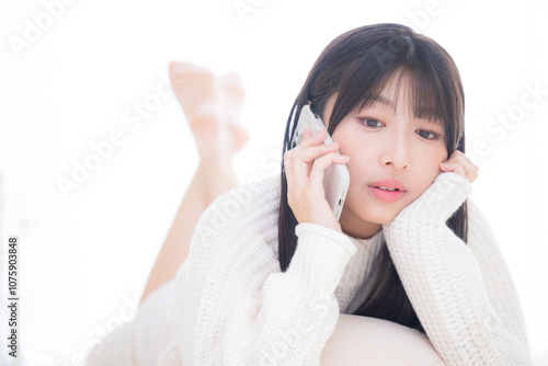 うつ伏せでスマホを通話するニットを着た若いかわいい女子のクローズアップ 返事を聞く、ダルイ驚く表情