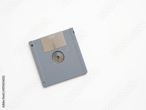 A single floppy disk lies isolated on a minimalist white surface, its color faded to a soft gray from years of exposure, computing history, floppy disk