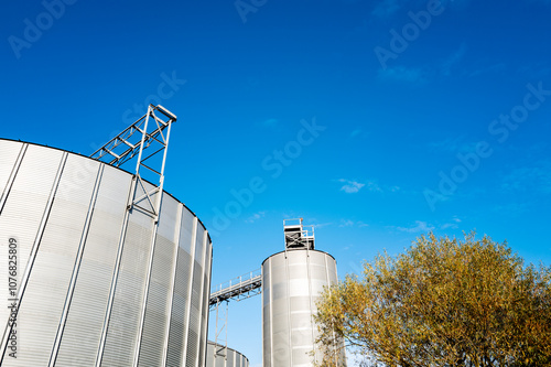 Bright metal grain silos seen against the autumn sun at a grain store and drying facility in the UK. The grain, winch dried is loaded and distributed to the food industry.