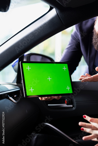 Informed salesperson answering questions in car dealership during test drive using green screen tablet. Sales executive offering advice to clients in search of new vehicle using mockup device