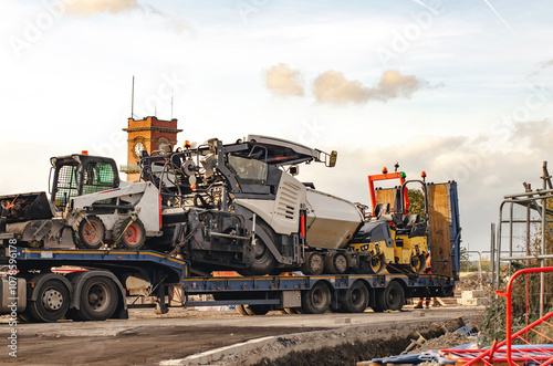 Construction vehicles loaded on a trailer at a construction site during the afternoon in an urban area