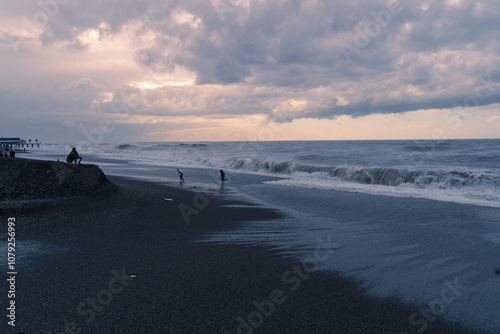 Evening on the shore of a stormy sea, people watching the sunset