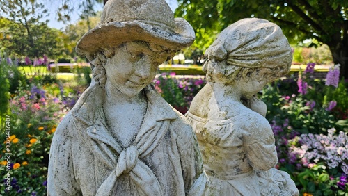 Faded white garden statue of a peasant boy and a shy girl in love, with flowers in the background