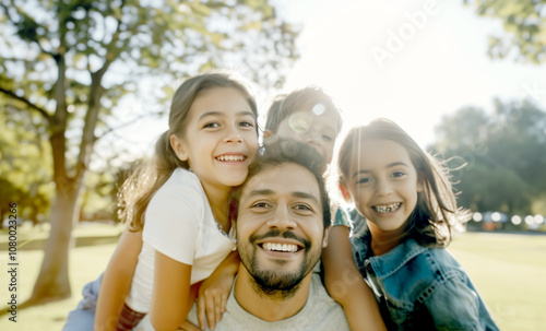 A happy family portrait featuring parents and their two young daughters smiling warmly while sitting together on a couch.