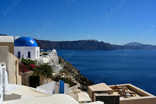 Eine Panoramaaussicht von Oia auf der griechischen Insel Santorin, zu einer der bekannten blauen Kuppelkirchen und den weiteren verlauf der Caldera bis nach Fira.