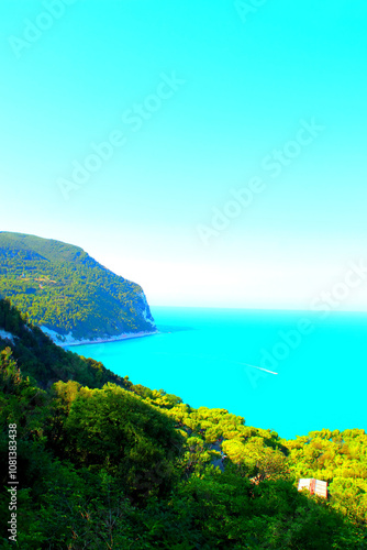 Impressive scenery from Piazzale Marino in Sirolo with corpulent green slope in the lower side of the picture culminating in Mount Conero and its vegetation standing on white rock between sea and boat