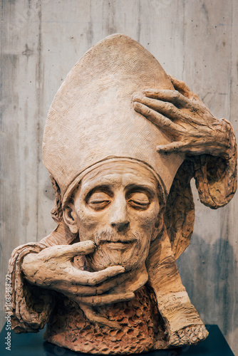 Tête d'évêque coiffé d'une mitre. Main sur un visage. Sculpture d'une tête de religieux 