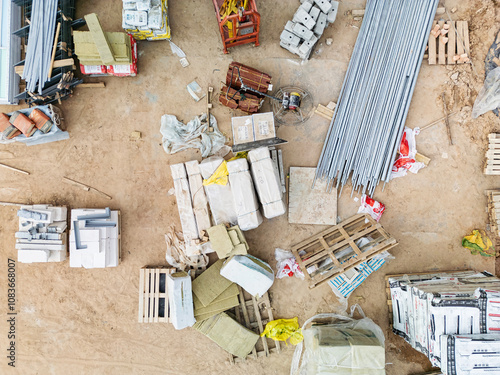 Construction materials strewn across a sandy ground at a bustling building site under clear blue skies during midday work hours