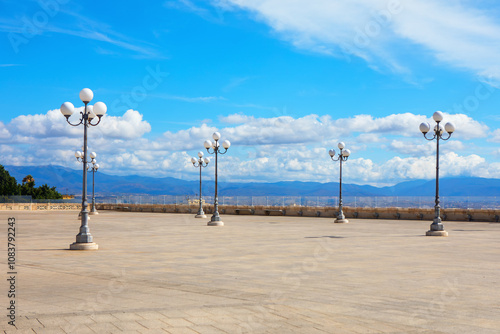 Expansive city plaza with ornate street lamps, light-colored stone tiles. Piazzetta David Herbert Lawrence in Cagliari Sardinia. Perfect for capturing public spaces and urban tranquility