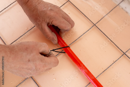 Installation of underfloor heating. A worker fastens pipes for underfloor heating made of cross-linked polyethylene to a reinforced mesh with clamps.