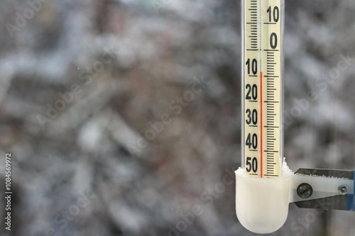 An outdoor thermometer shows sub-zero temperatures in winter in December against the backdrop of snow-covered trees