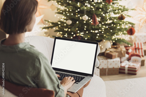 Young woman using laptop computer with blank empty mockup screen during Christmas holidays at home, Online shopping at winter holidays, ordering Christmas gifts, Website template.