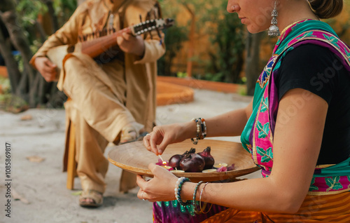 Indian musician in traditional clothes playing sitar festive season outdoor home. Woman in traditional saree hand lighting Diya lamp during Diwali festival. Happy greeting photo. Part of a series