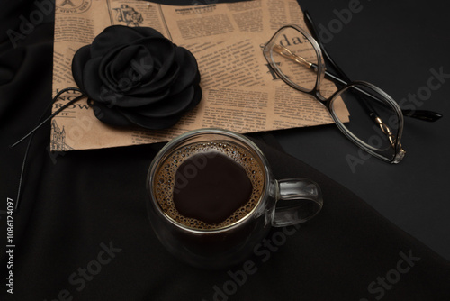 Black coffee in a lighted cup with additional elements and a black background.