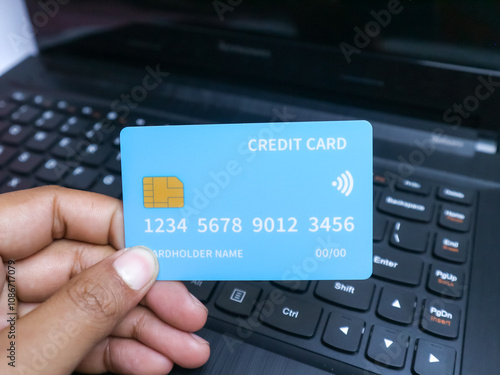 hand holding a credit card with a visible chip and contactless symbol, shown over a laptop keyboard, symbolizing online payment or financial transactions