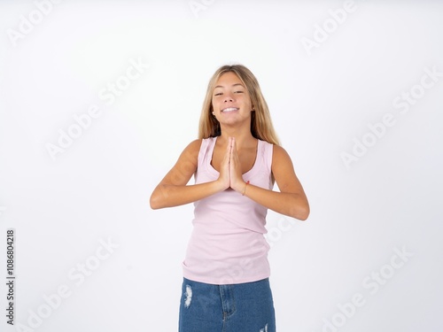 Beautiful teen girl wearing sleeveless t-shirt praying with hands together asking for forgiveness smiling confident.