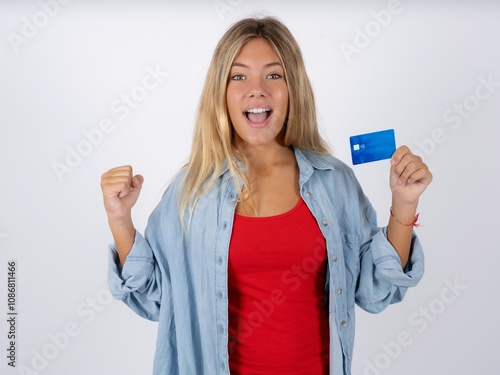 Photo of lucky impressed Beautiful teen girl wearing denim jacket arm fist holding credit card. Celebrated