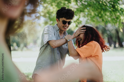 Cheerful friends enjoying a playful moment, messing up each other's hair and laughing together in a sunny park.