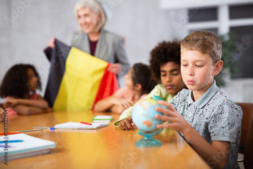 Friendly female teacher working in a high school tells pupils the history of Belgium in class and holds the national flag of .the country in her hands