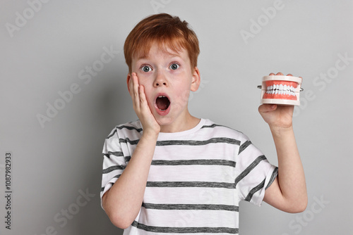 Dental phobia. Scared boy with model of jaw on grey background