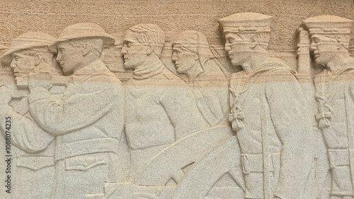 A stone relief shows a group of WWI soldiers and sailors in uniform, walking in unison with detailed expressions and attire, symbolizing unity and service in a historical commemorative artwork.