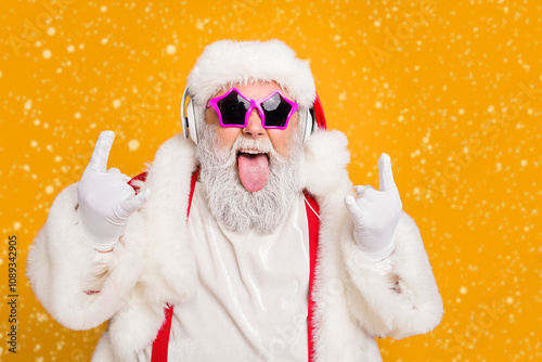 Close up photo of crazy funny hipster santa claus show horns sign tongue-out want rock-and-roll concert instead x-mas tradition celebration wear hat trendy suspenders isolated yellow color background