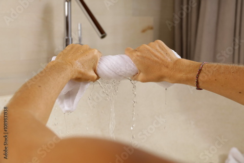 A person wringing out a wet towel over a bathtub.