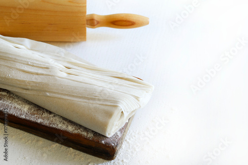 Pasta fillo fresca su un tagliere di legno infarinato e un mattarello isolato su un tavolo di legno bianco. Copia spazio.