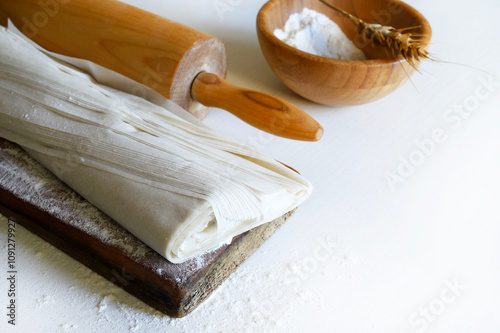 Pasta fillo fresca su un tagliere di legno infarinato e un mattarello isolato su un tavolo di legno bianco. Copia spazio.