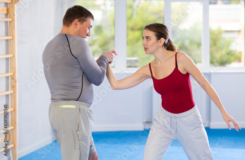 Aggressive young girl and middle-aged man practicing arm twist technique during self-defense courses