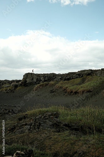 Solitary figure on a rocky cliff under a vast sky.